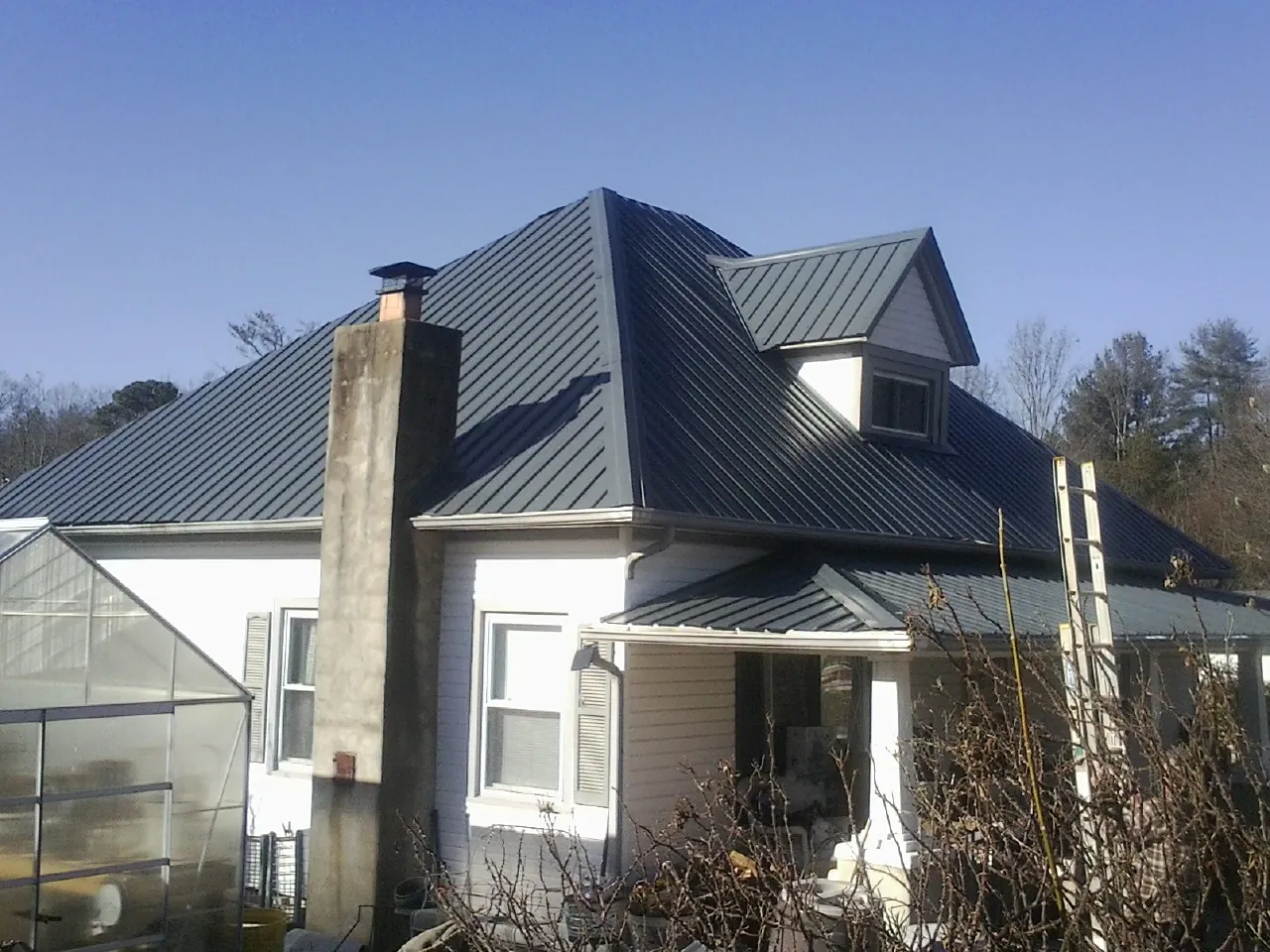 Dark blue standing seam metal roof on a white farmhouse with dormer — Slate & Tile Roof Repair by Roofing Brothers in Altair