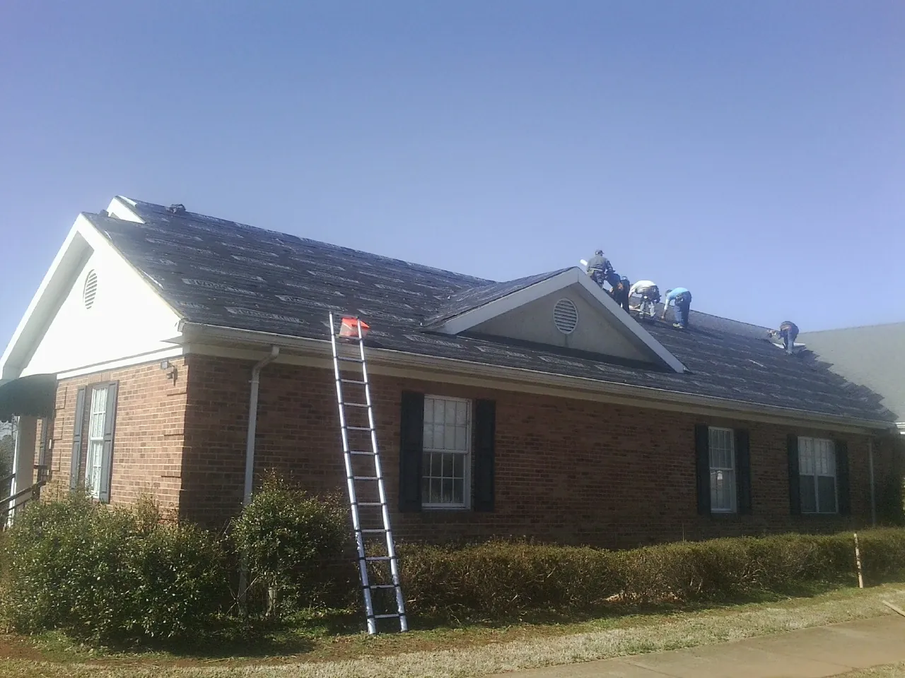 Crew tearing shingles off a brick ranch roof with a ladder set — Emergency Roof Repair work by our crew in Altair