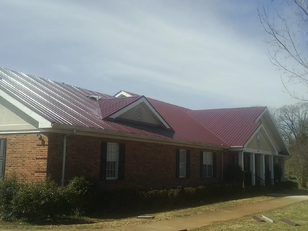 Red metal roof with gabled entries on a long brick building, from a Hail Damage Roof Repair job in Altair