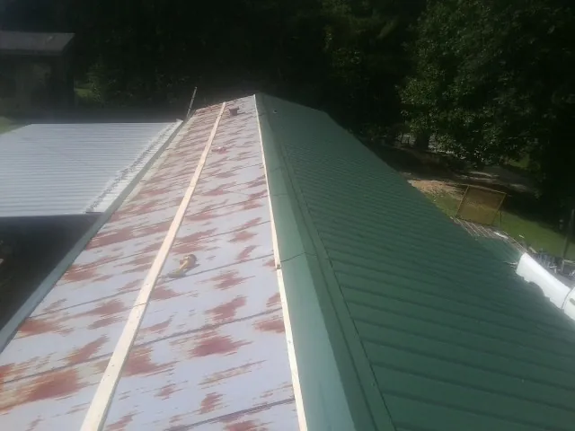 Old rusted panels beside newly installed green metal roofing — Wind Damage Roof Repair by Roofing Brothers in Altair