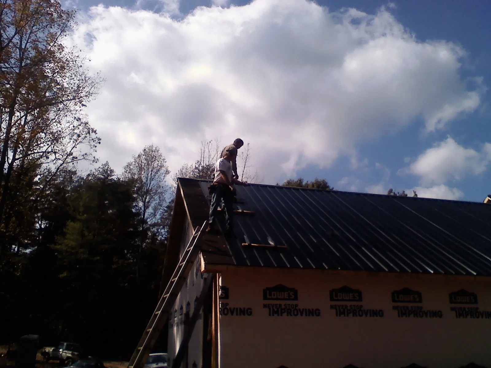 Roofer fastening dark metal panels high against a cloudy sky, from a Roof Inspection job in Altair