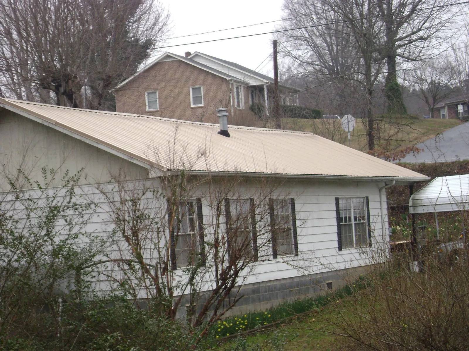 Tan metal roof on a white sided house set into a hillside — Commercial Roofing by Roofing Brothers in Altair