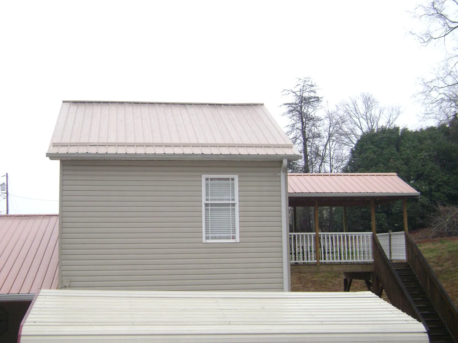 Tan metal roofs on a two story addition and attached porch, from a Roof Replacement job in Altair